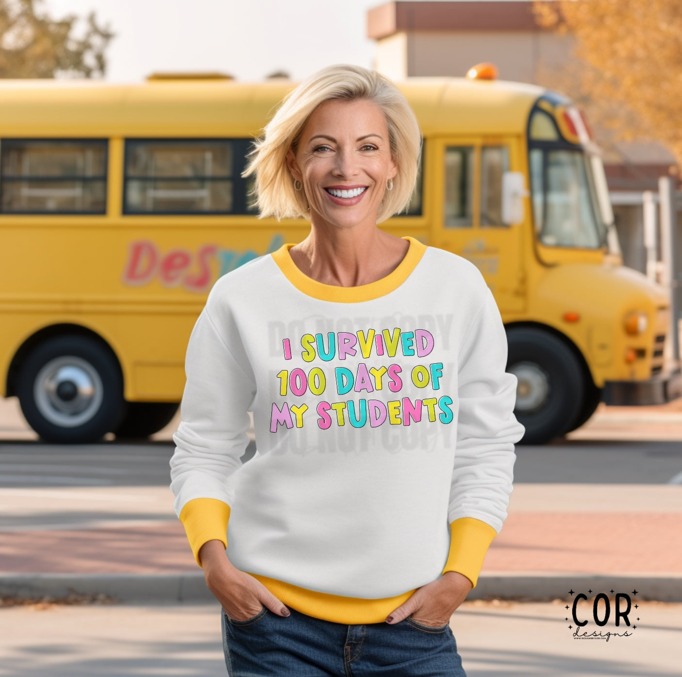 A person wearing a white long-sleeve t-shirt with a colorful text graphic that reads 'I SURVIVED 100 DAYS OF MY STUDENTS' on the front, standing next to a yellow school bus.