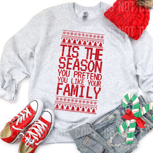 a sweatshirt with tis the season you pretend to like your family on it with christmas clothing an packages around it