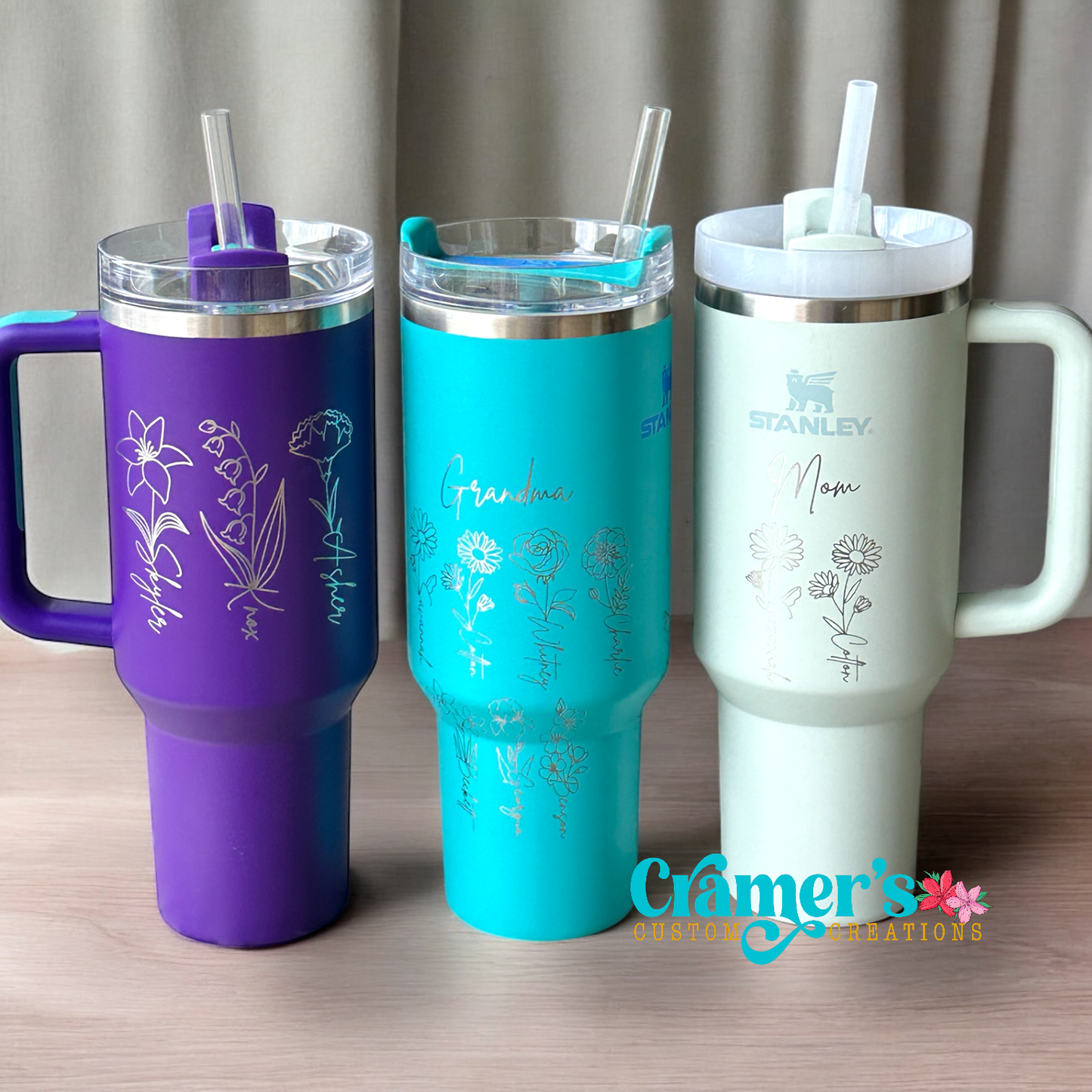 Three insulated tumblers with straws, each in different colors: purple, blue, and white, all featuring engraved birth month flowers and names.