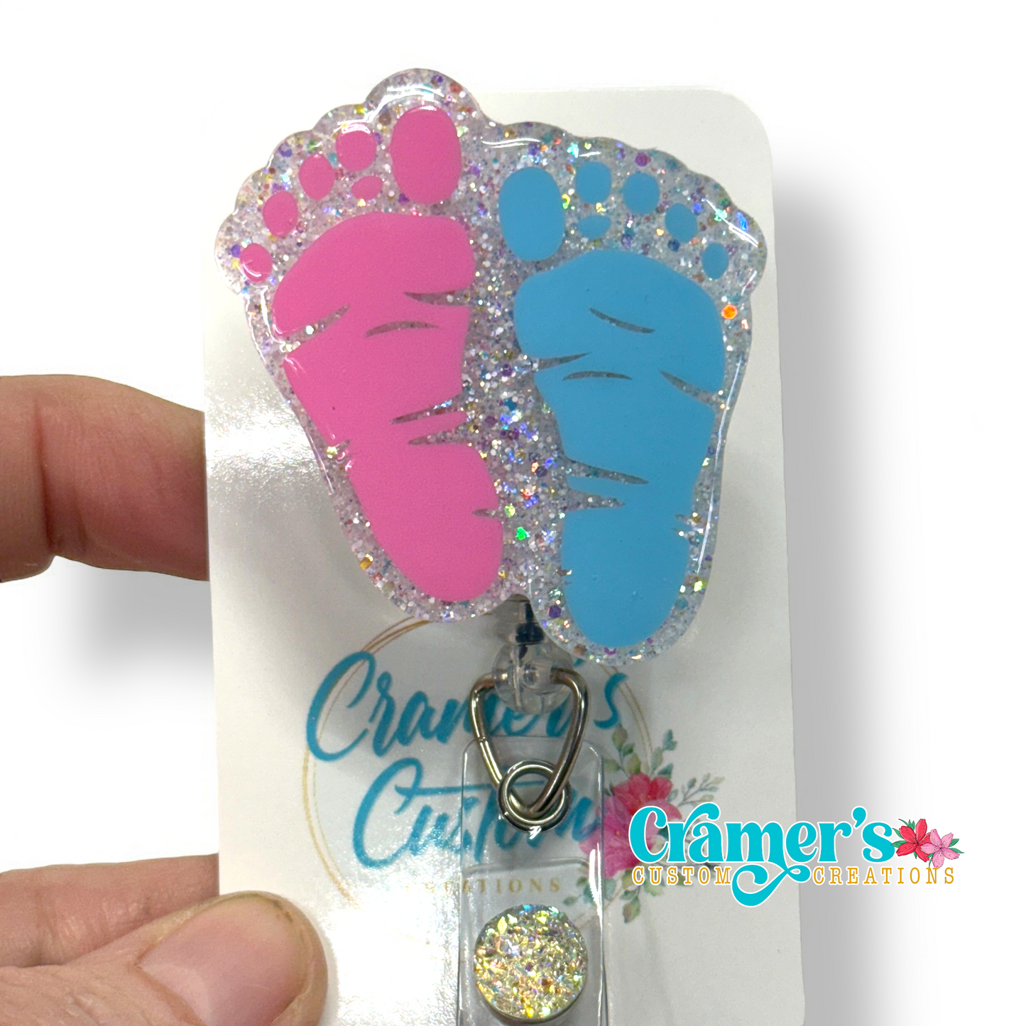 badge reel of two footprints one pink one blue with a white glitter backgound