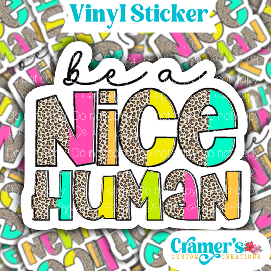 Sticker laying flat that says be a nice human on a background of the same sticker stacked up