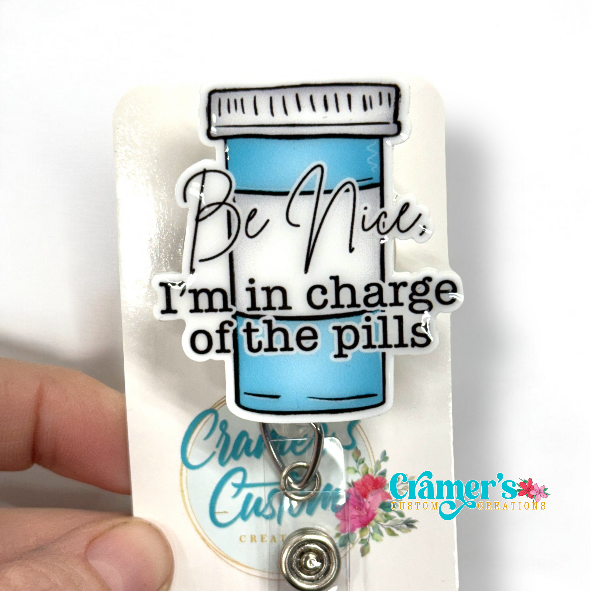 badge reel showing a non glitter option of a badge with a pill bottle with the words be nice, i'm in charge of the pills