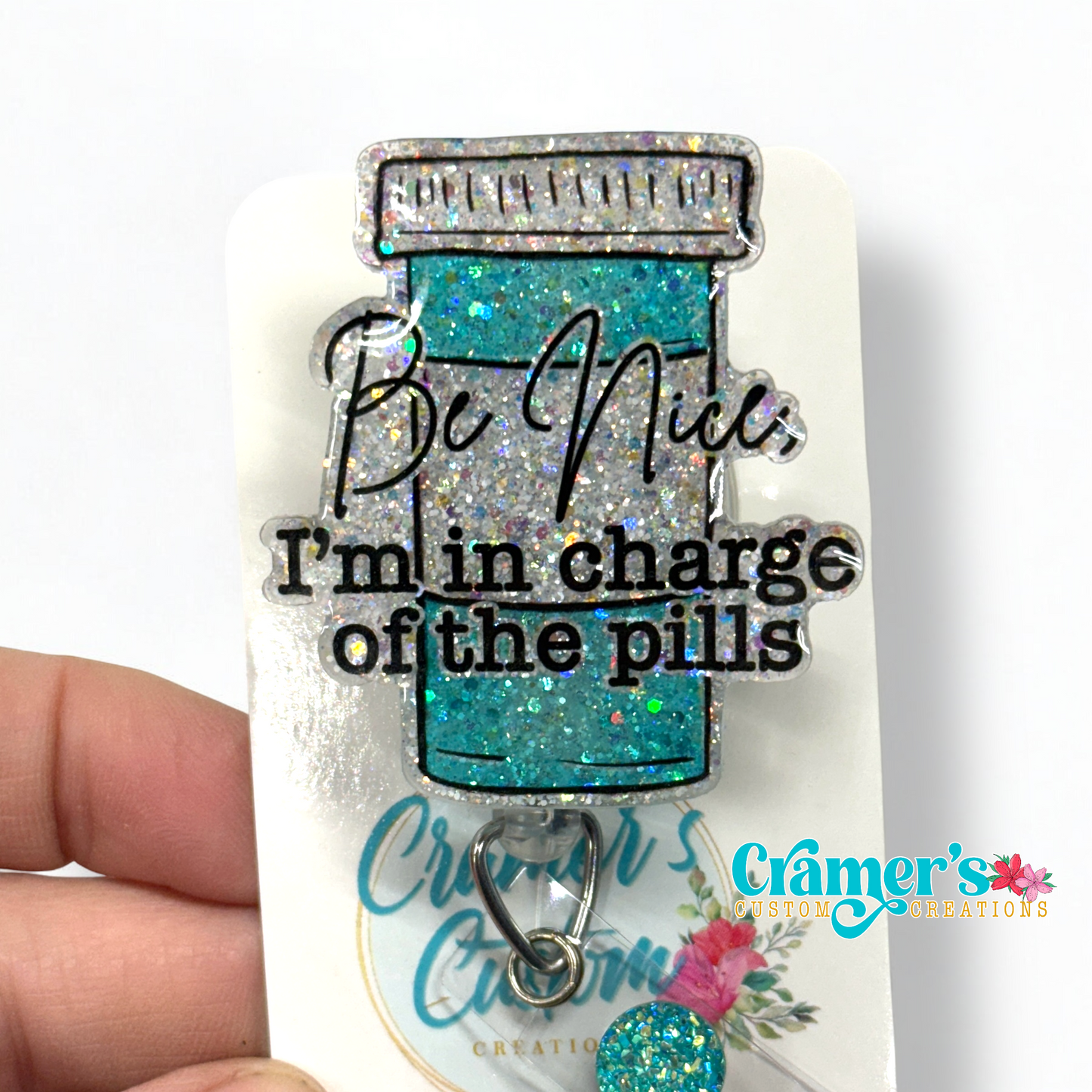 badge reel showing a glitter option of a badge with a pill bottle with the words be nice, i'm in charge of the pills