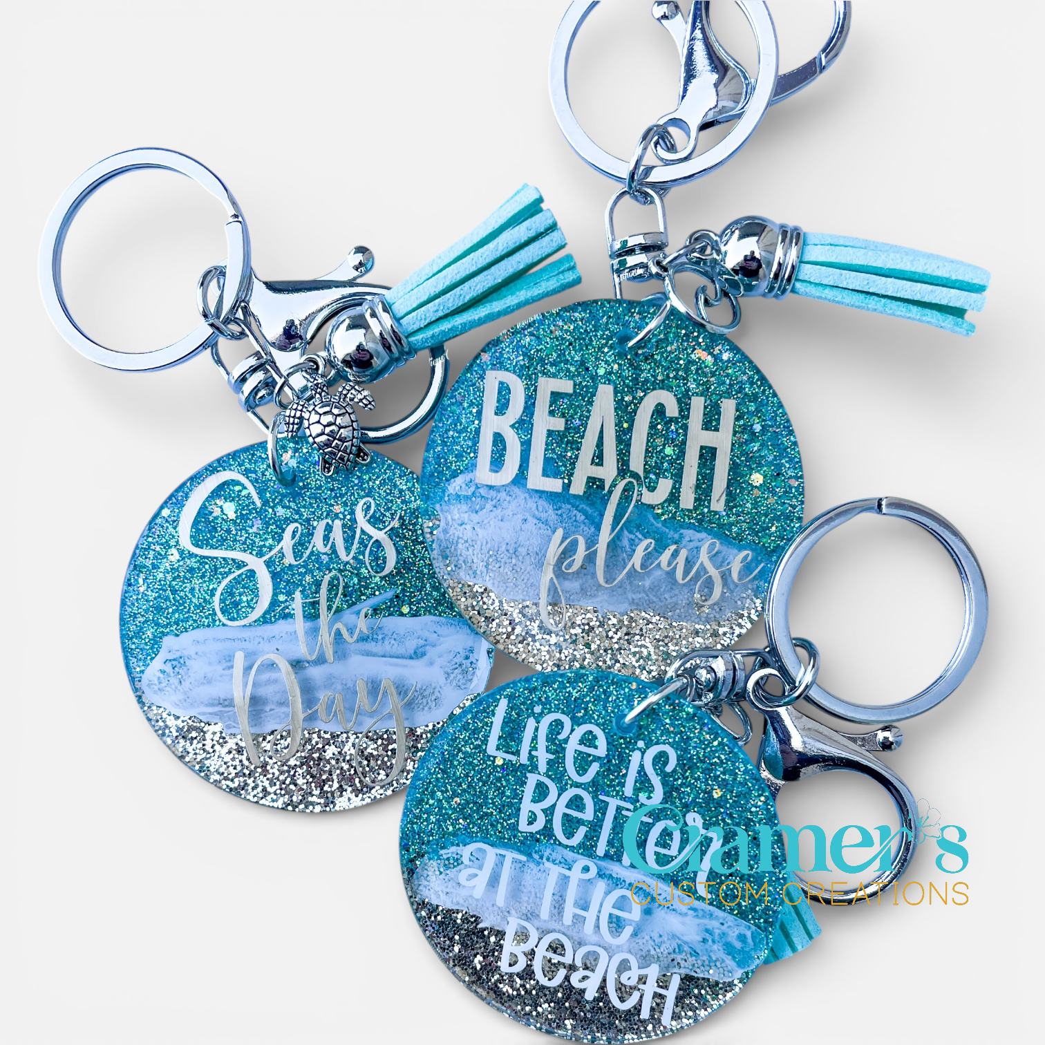 Three keychains with beach-themed phrases and tassels on a white background