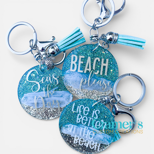 Three keychains with beach-themed phrases and tassels on a white background