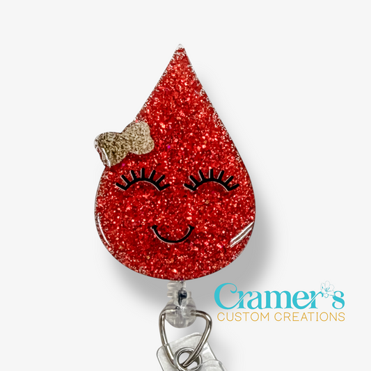 Red glittery badge holder shaped like a teardrop with a face design on a white background, featuring the brand 'Cramer's Custom Creations'.