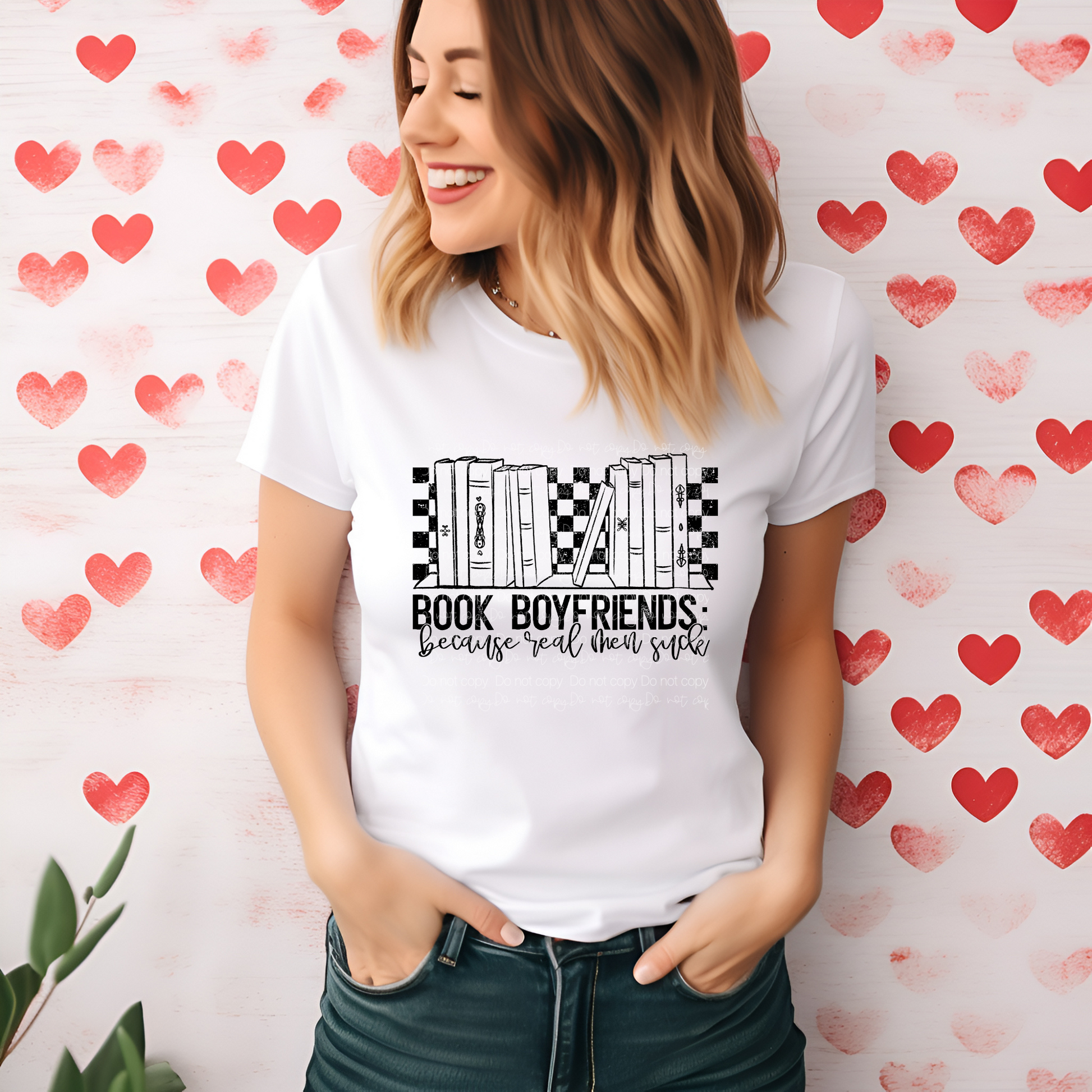A person smiling and wearing a white t-shirt with a printed text that reads 'BOOK BOYFRIENDS because you're too cool to be just a friend' on the front, against a heart-patterned background.