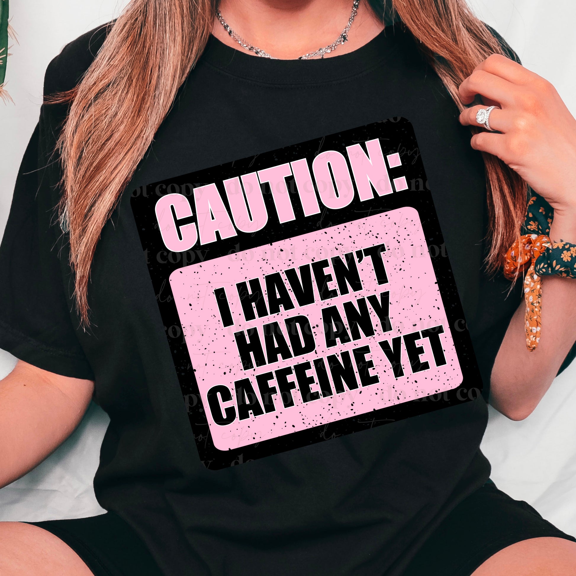 A person wearing a black t-shirt with the text 'CAUTION: I HAVEN'T HAD ANY CAFFEINE YET' in pink lettering.