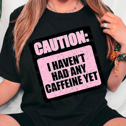 A person wearing a black t-shirt with the text 'CAUTION: I HAVEN'T HAD ANY CAFFEINE YET' in pink lettering.