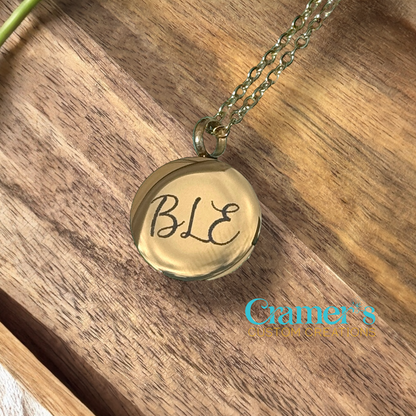 Gold necklace with 'BLE' pendant on a wooden surface, brand 'Gamer's' visible.