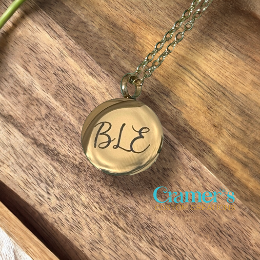 Gold necklace with 'BLE' pendant on a wooden surface, brand 'Gamer's' visible.