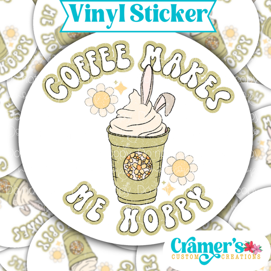 Sticker laying flat that says coffee makes me hoppy with bunny ears on a coffee on a background of the same sticker stacked up