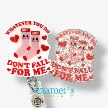 2 badge reels showing a glitter and a non glitter option of a badge with pink socks and hearts that says whatever you do, don't fall for me