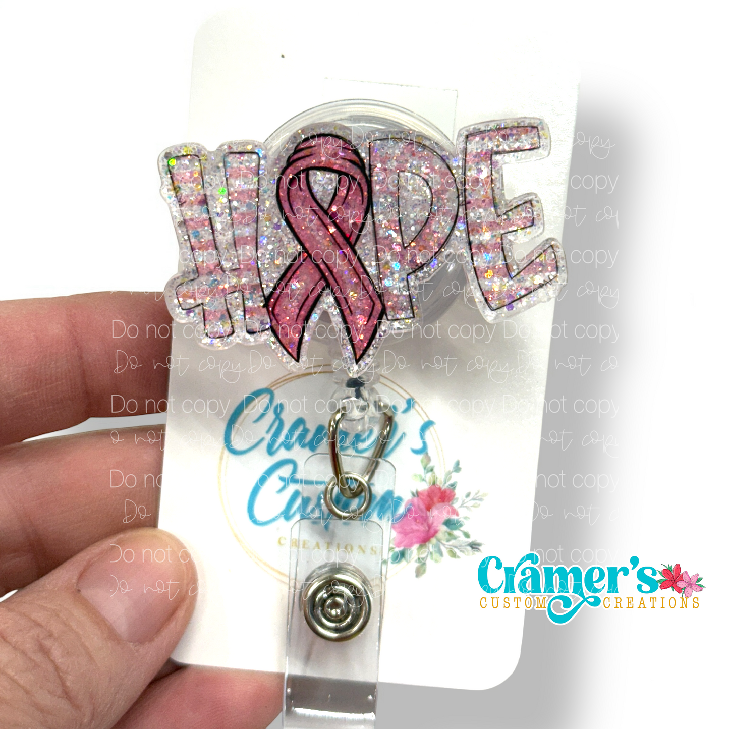 A badge reel showing the word hope with a ribbon as the letter O with a pink color and glitter back ground