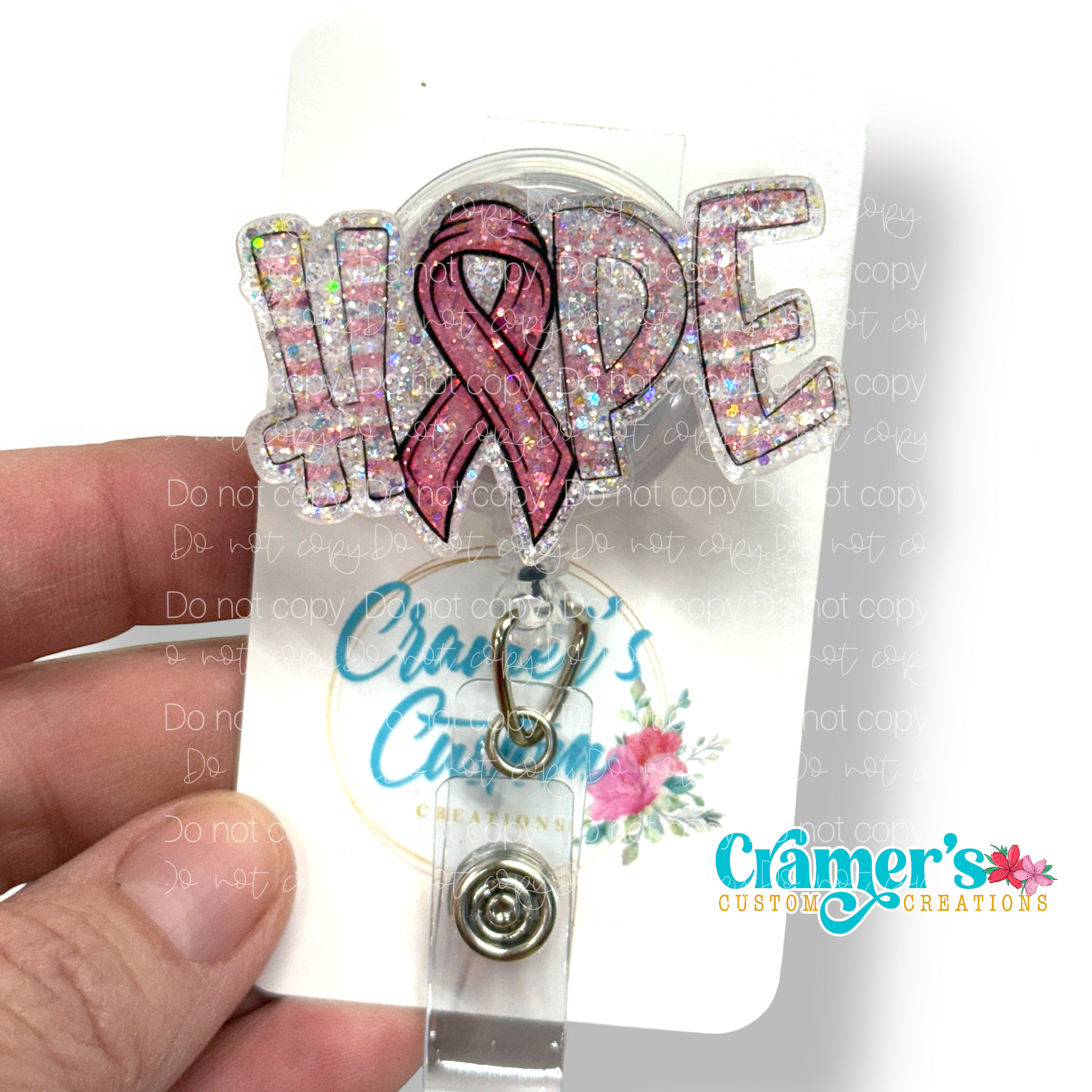 A badge reel showing the word hope with a ribbon as the letter O with a pink color and glitter back ground