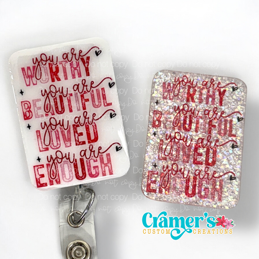 2 badge reels showing a glitter and a non glitter option of a badge with the words you are worthy you are beautiful, you are loved, you are enough in pink and red text