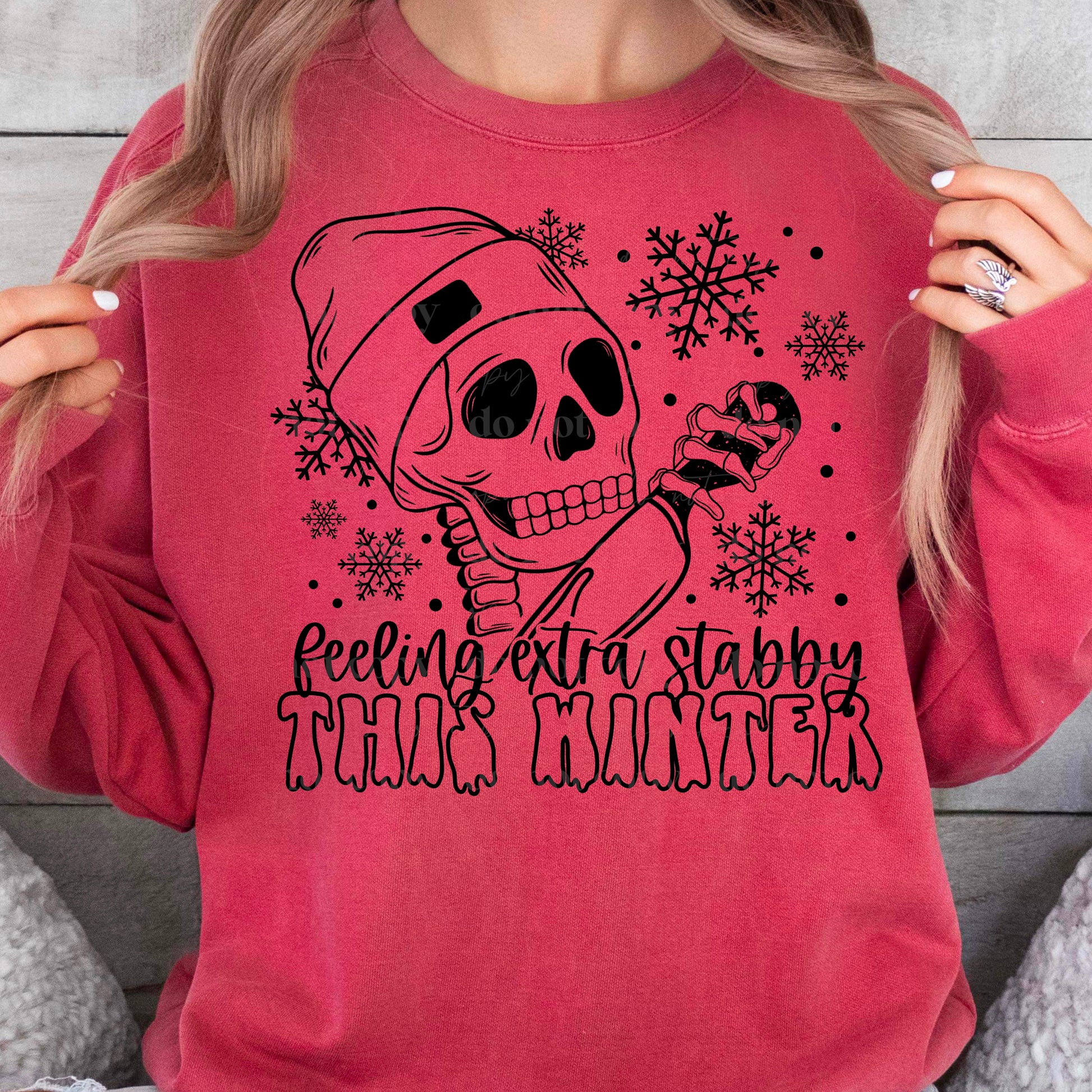 A pink t-shirt with a black and white skeleton design, surrounded by snowflakes, and the text 'Feeling Extra Stabby this Winter'.
