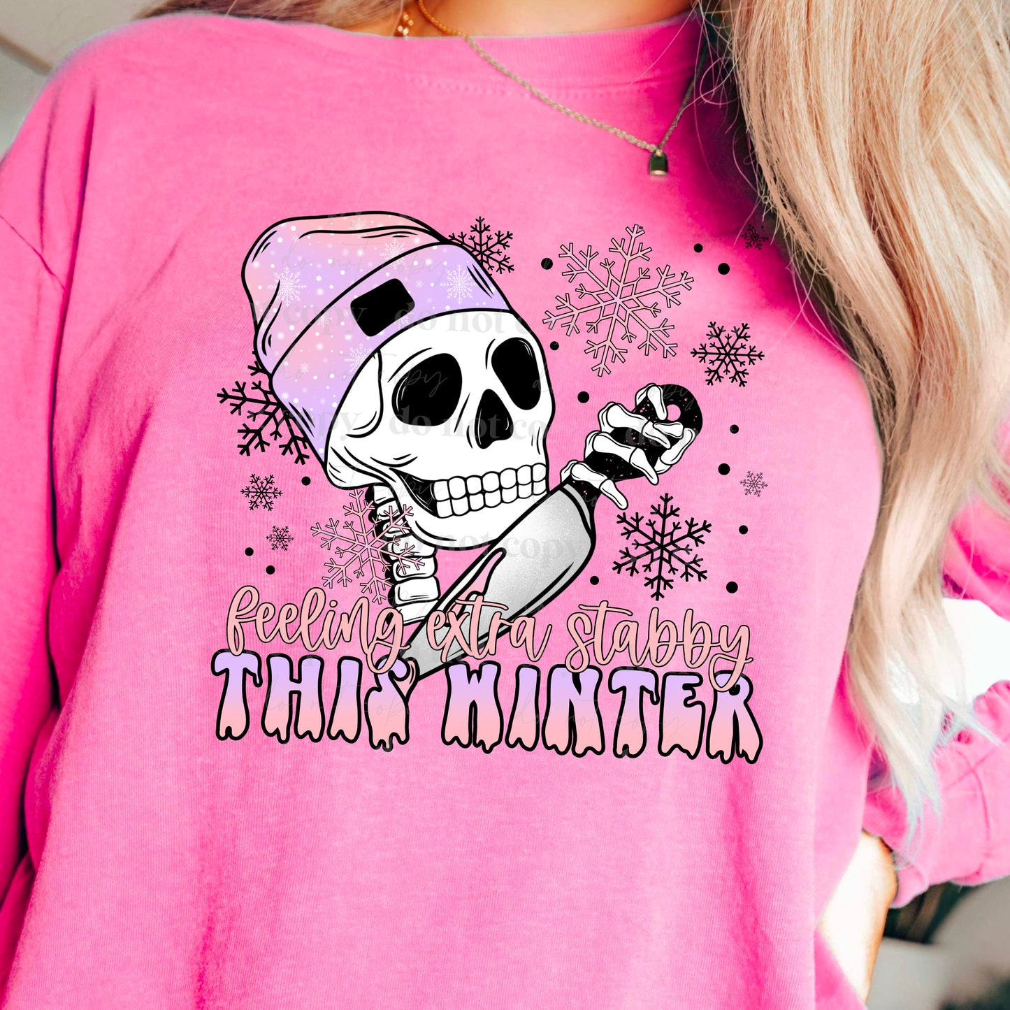 woman wearing a pink shirt that has a skeleton head wearing a beanie holding a knife that says feeling extra stabby this winter