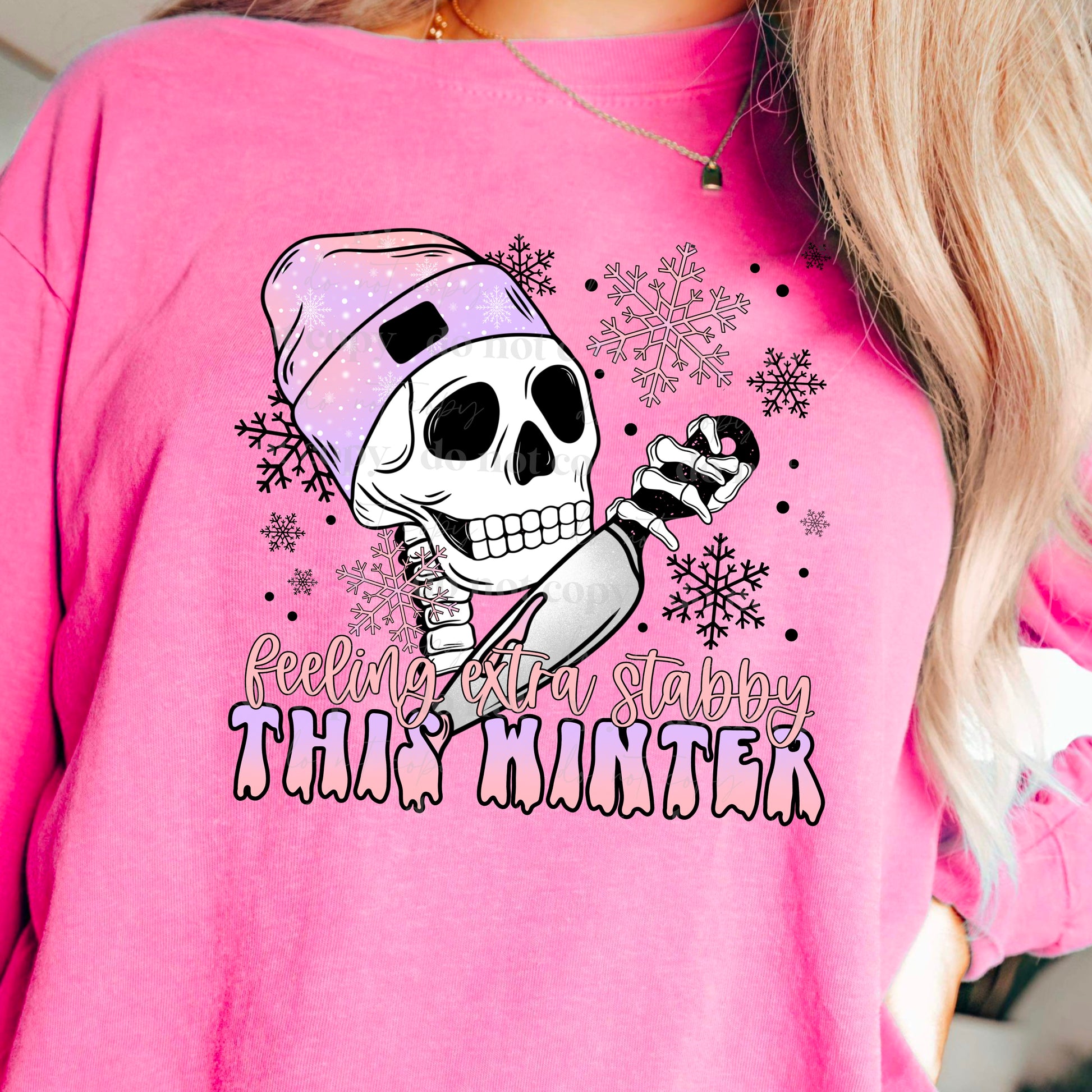 woman wearing a pink shirt that has a skeleton head wearing a beanie holding a knife that says feeling extra stabby this winter