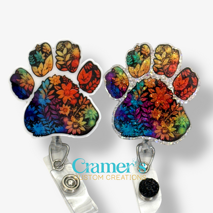 2 badge reels showing a glitter and a non glitter option of a rainbow colored floral paw print
