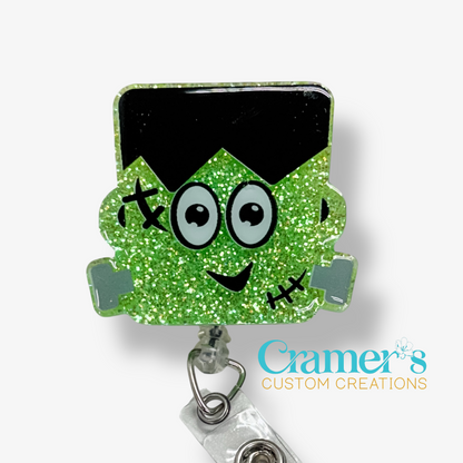 Green glittery monster head badge holder with black hair on a white background, featuring the brand 'Cramer's Custom Creations'.