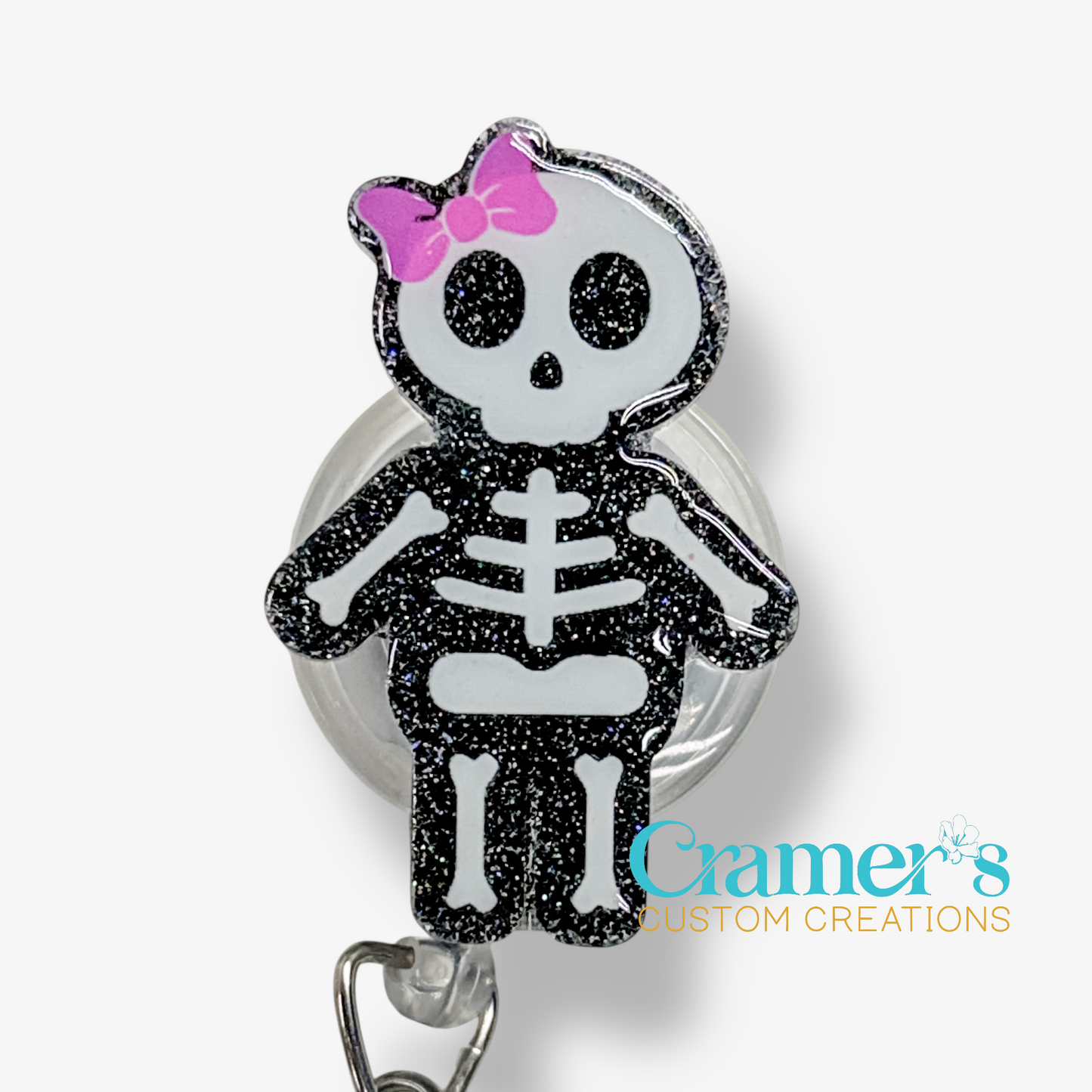 Skeleton character with a pink bow on a badge holder against a white background, branded 'Cramer's Custom Creations'.