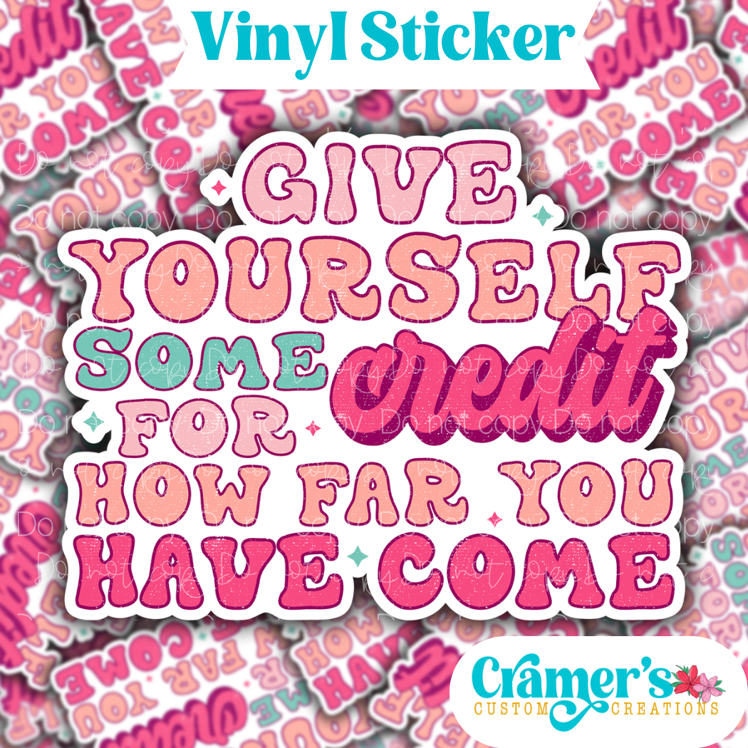 Sticker laying flat that says give yourself some credit for how far you have come on a background of the same sticker stacked up