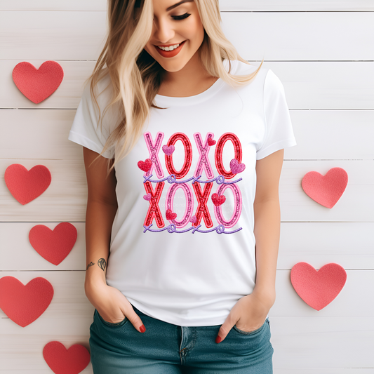 A person wearing a white t-shirt with the text 'XOXO' in pink glitter print.