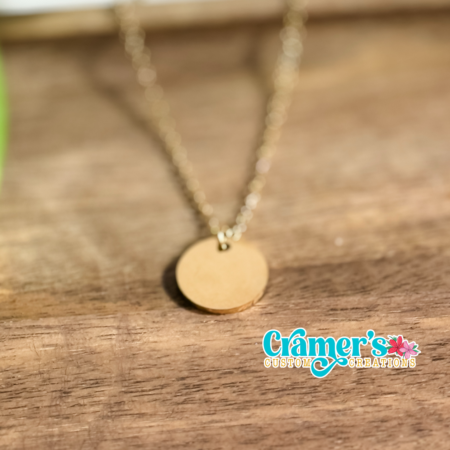 A 15 mm circular pendant necklace in gold color, displayed on a wooden surface.