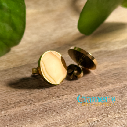 a pair of gold circle stud earrings on a wood background
