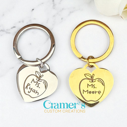 Two keychains with engraved names on heart-shaped tags against a marble background.