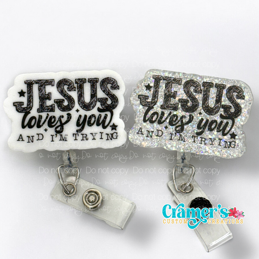 Two badge reels with acrylic coating and high quality glitter, one with a silver clip and the other with a black clip, both with the text 'JESUS LOVES YOU AND I'M TRYING' written in a bold, black font, surrounded by sparkle accents.