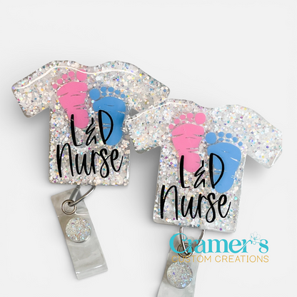 badge shaped like a scrub top with white glitter, a pink and a blue foorprint, and the words 'L&D Nurse'