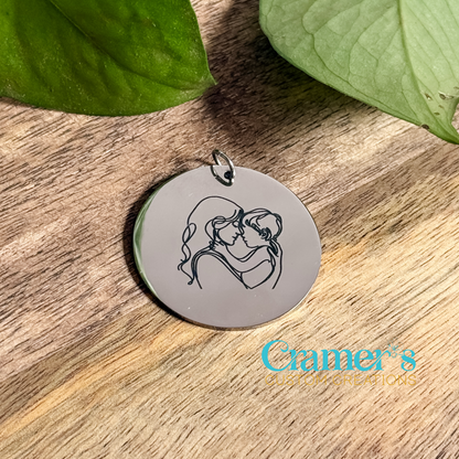 Stainless steel pendant with engraved design on a wooden surface with leaves