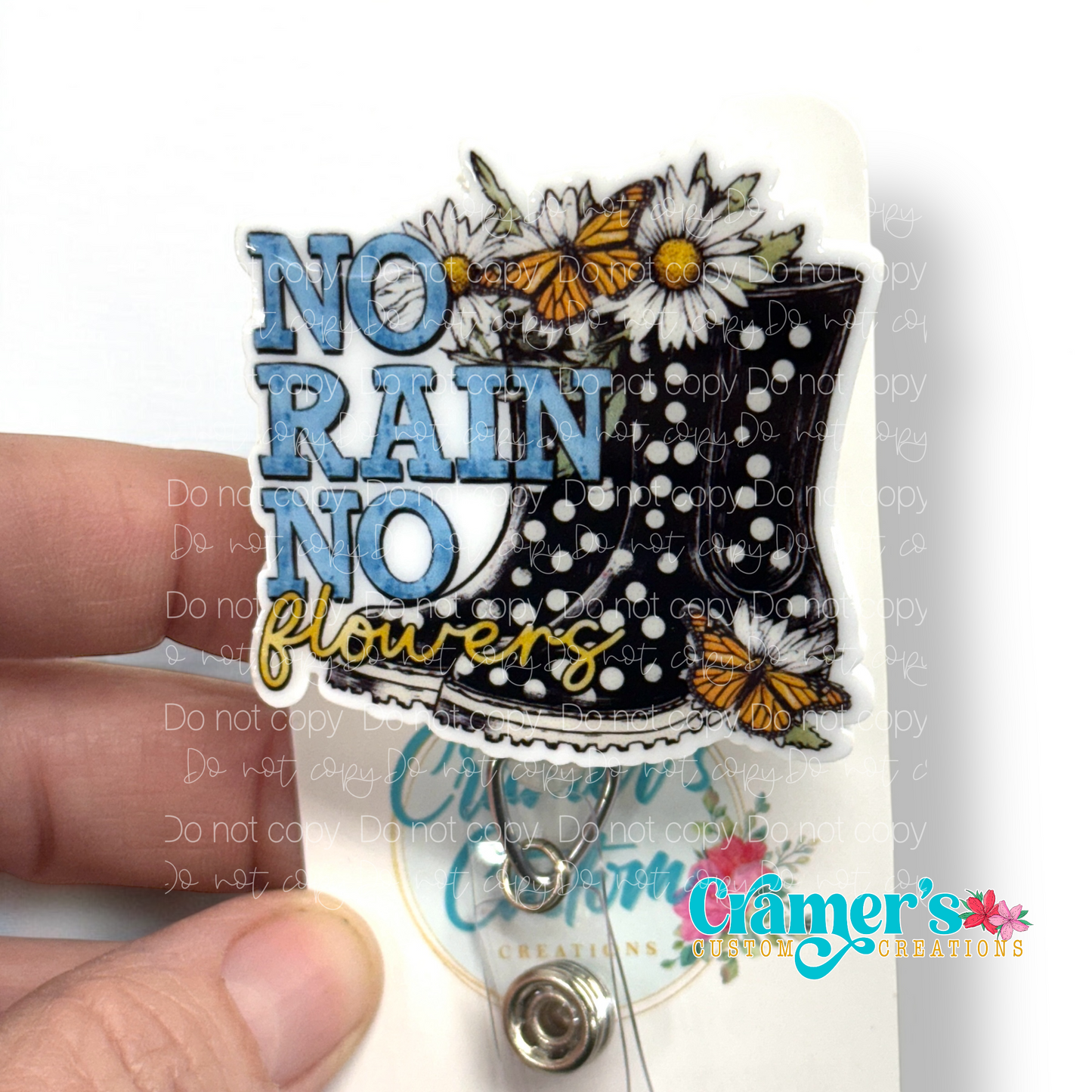 badge reel showing a non glitter option of a boot with flowers and butterflies that says no rain, no flowers