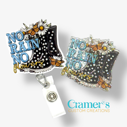 2 badge reels showing a glitter and a non glitter option of a boot with flowers and butterflies that says no rain, no flowers
