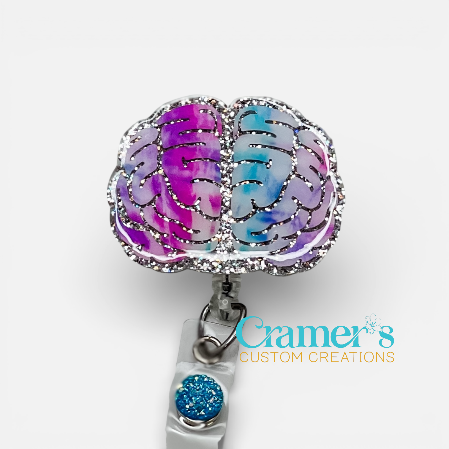 Colorful brain-shaped badge holder with a blue glitter accent on a white background, featuring the brand 'Cramer's Custom Creations'.