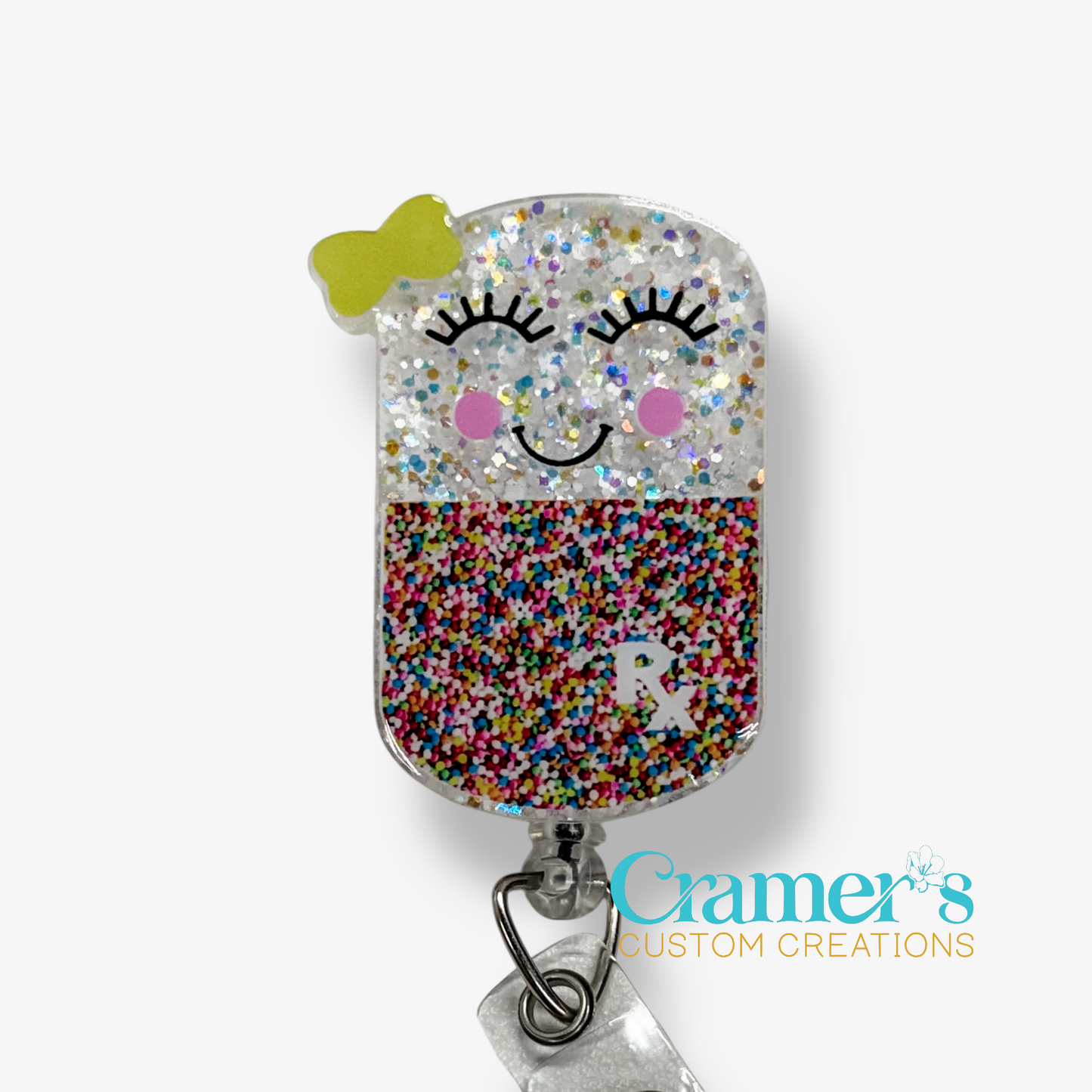 Glittery badge holder with cartoon face design on a white background, featuring the brand 'Cramer's Custom Creations'.