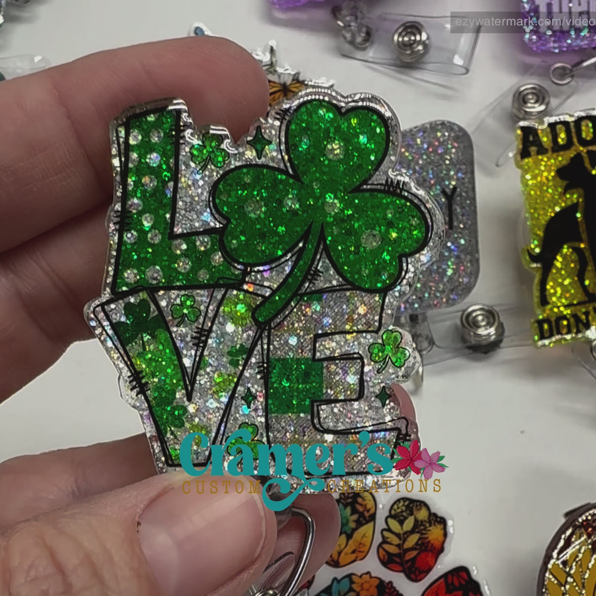 Video of 2 badge reels showing a glitter and a non glitter option of a badge with the word love with a shamrock being the O