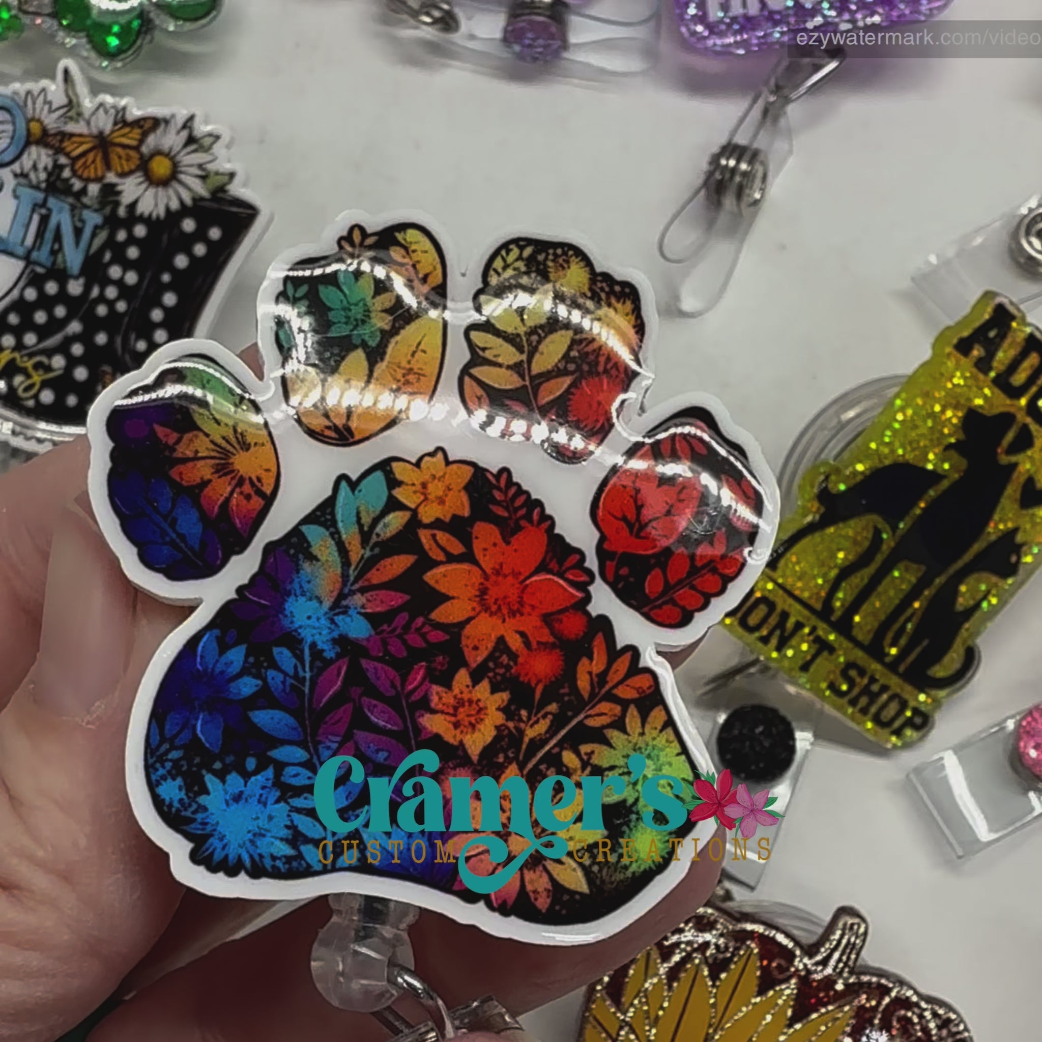 Video of 2 badge reels showing a glitter and a non glitter option of a rainbow colored floral paw print