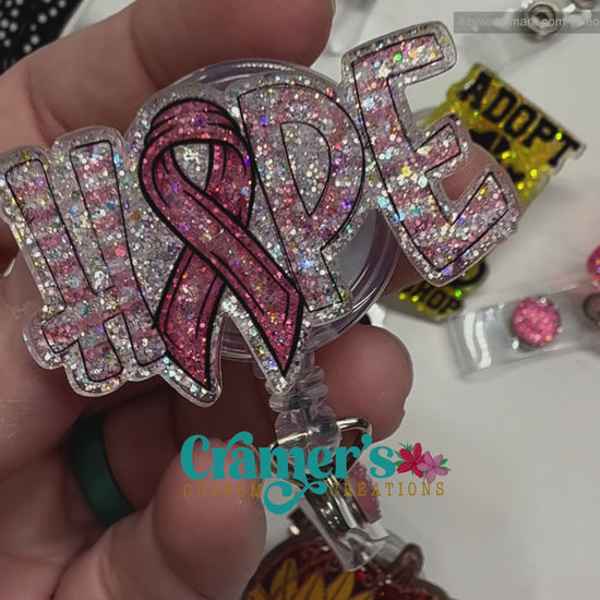 video of A badge reel showing the word hope with a ribbon as the letter O with a pink color and glitter back ground