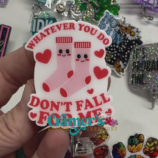 video  of 2 badge reels showing a glitter and a non glitter option of a badge with pink socks and hearts that says whatever you do, don't fall for me