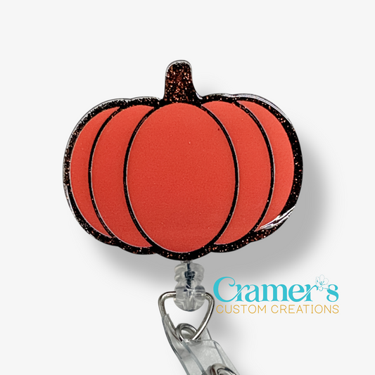 Pumpkin-shaped badge holder with glittery texture on a white background, featuring the brand 'Cramer's Custom Creations'.