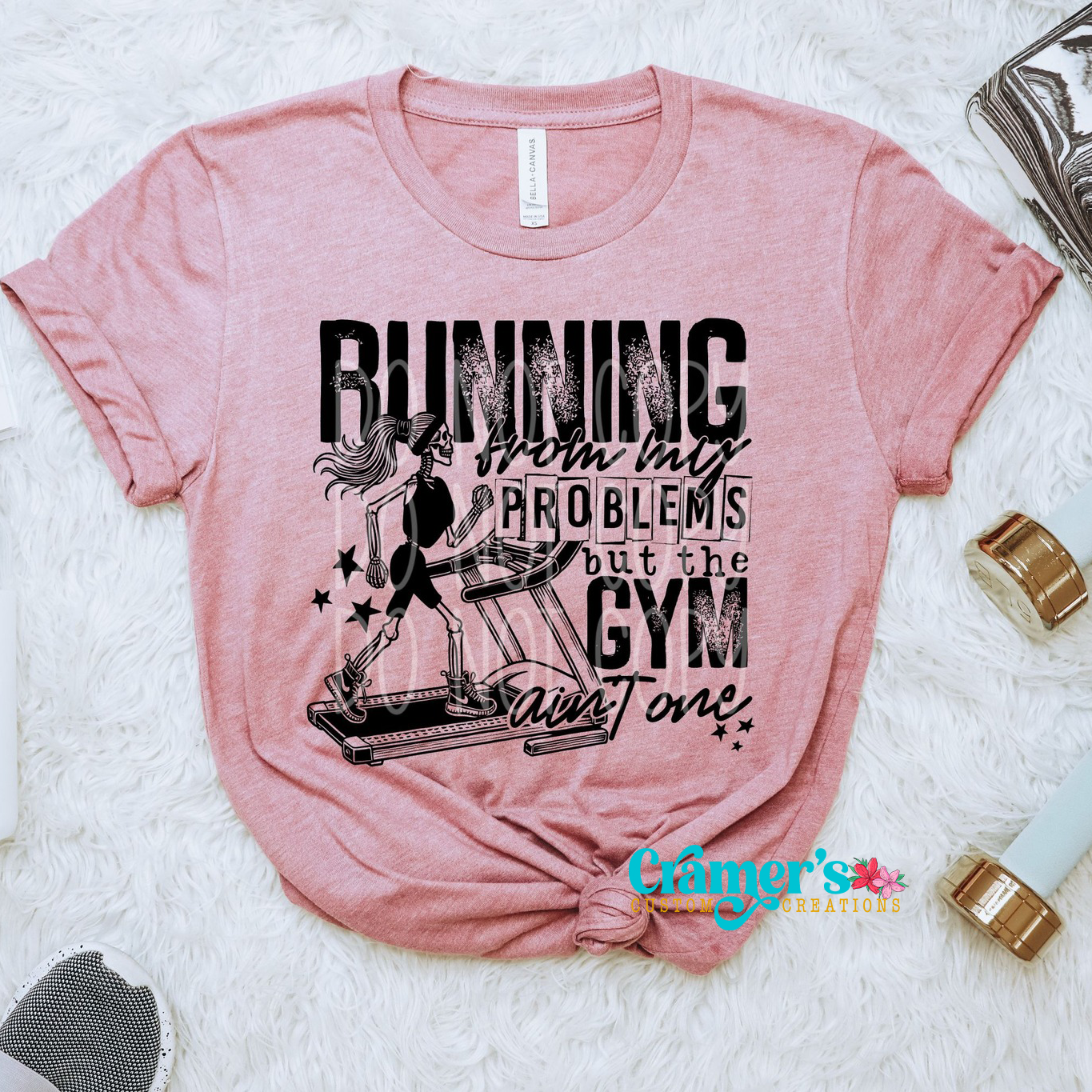 a pink shirt flat lay with a skeleton running on a treadmill that says running from my problems but the gym aint one