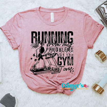 a pink shirt flat lay with a skeleton running on a treadmill that says running from my problems but the gym aint one