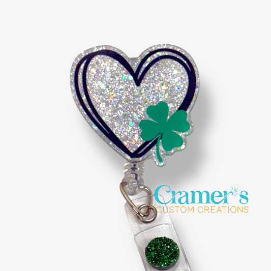Heart-shaped badge holder with a green shamrock on a white background, featuring the brand 'Cramer's Custom Creations'.