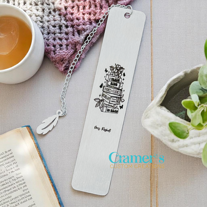Stylized bookmark with a decorative chain, placed on a textured surface with a cup of tea and plant.