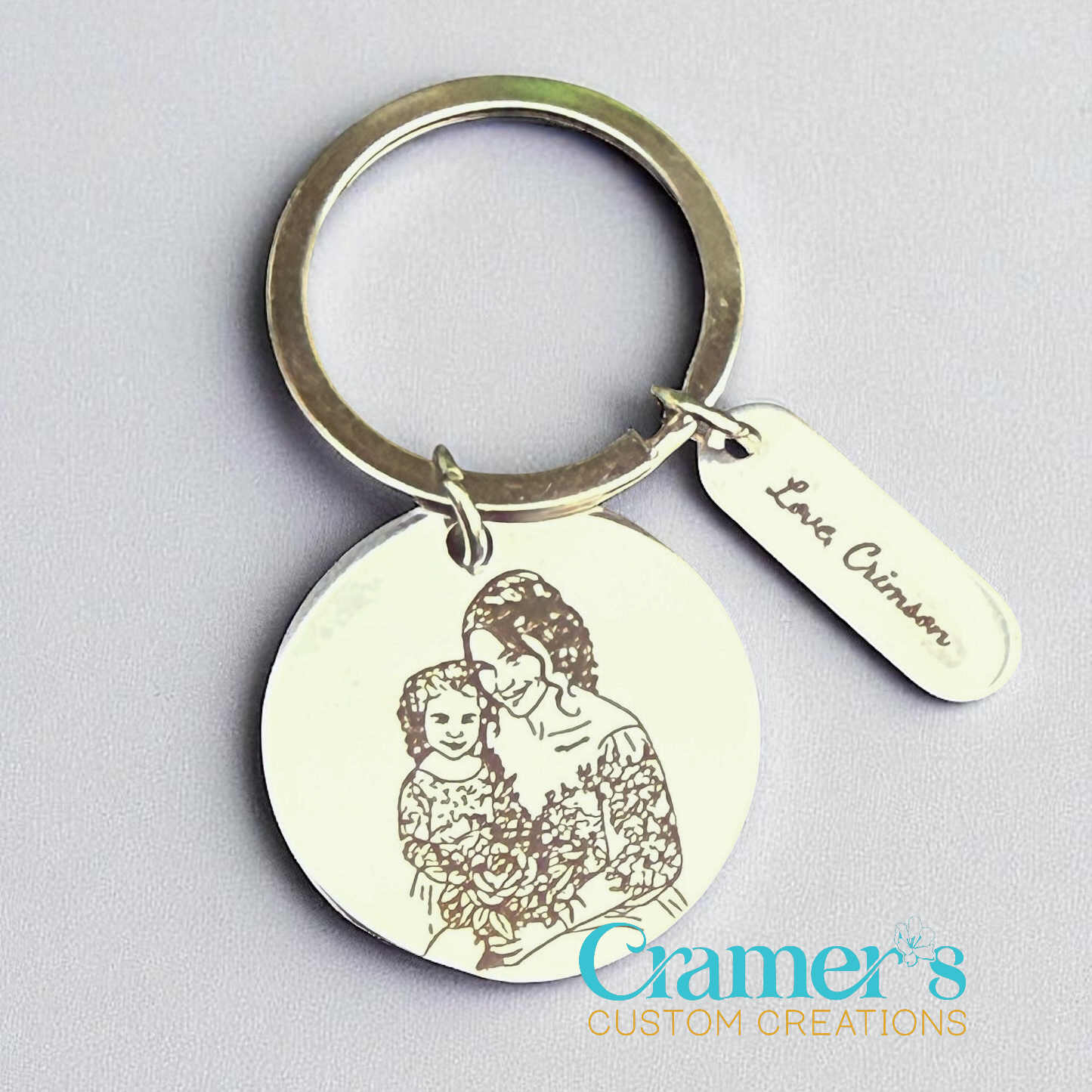 Keychain with engraved image of a woman and child, and a tag reading 'Lana Crimson'. Brand 'Cramer's Custom Creations' visible.