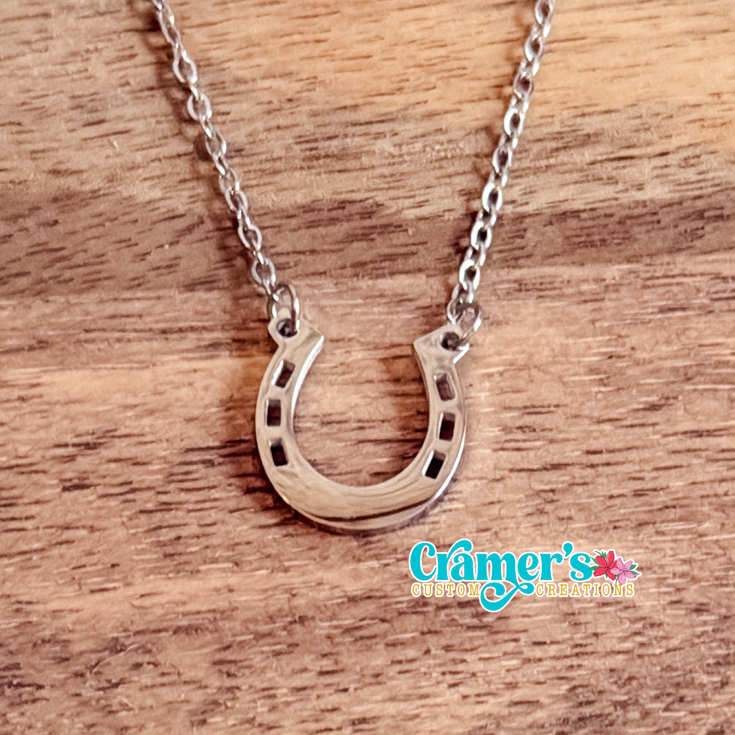 Silver horseshoe necklace on a wooden surface with 'Cramer's Custom Creations' branding.