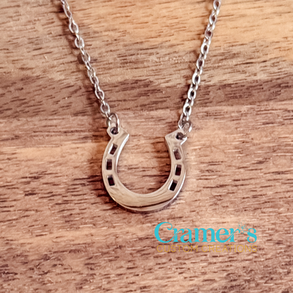Silver horseshoe necklace on a wooden surface with 'Cramer's Custom Creations' branding.